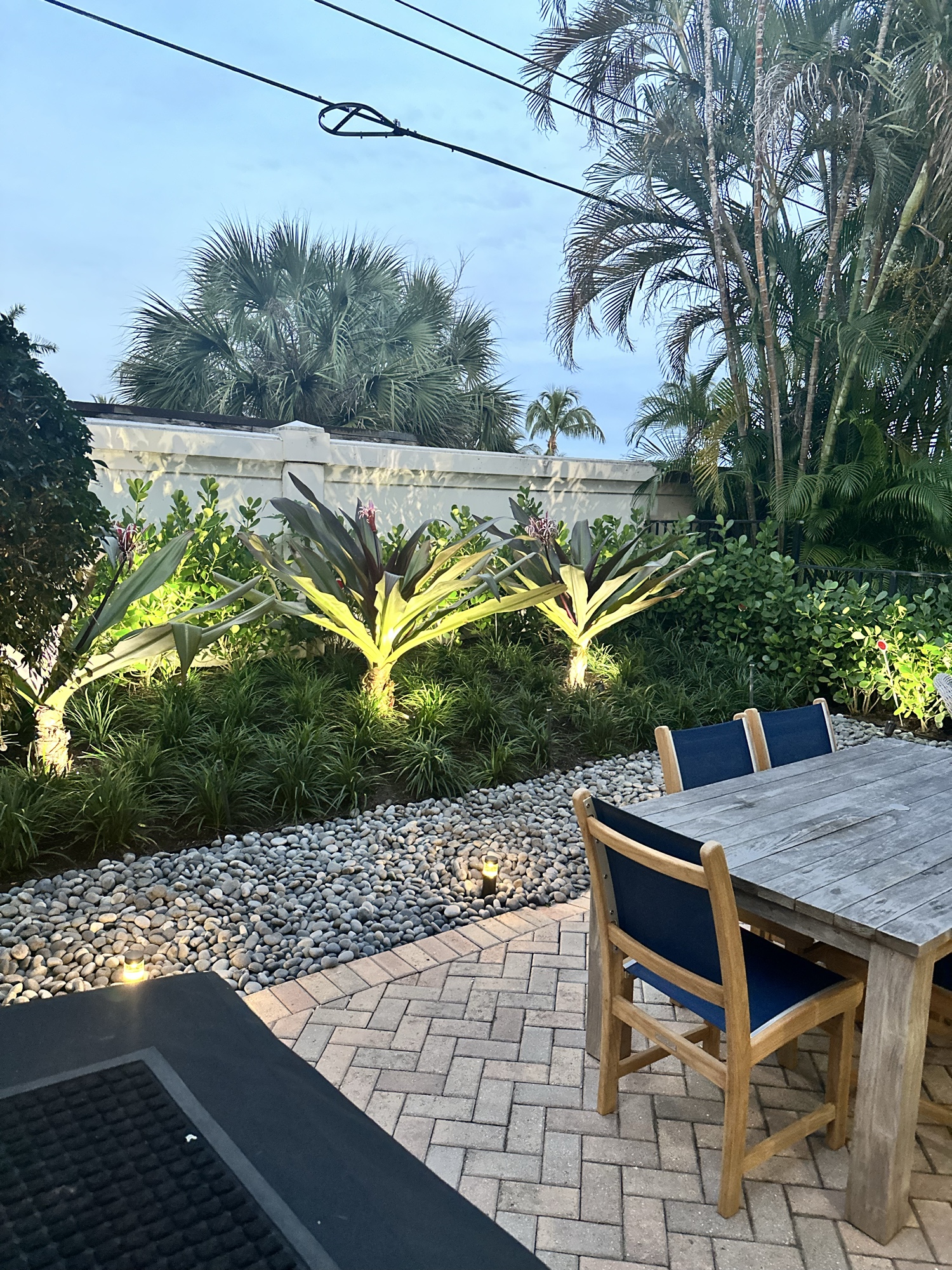 Luxury landscape uplighting at dusk — tropical palms and hardscape lit from below with warm accent lights